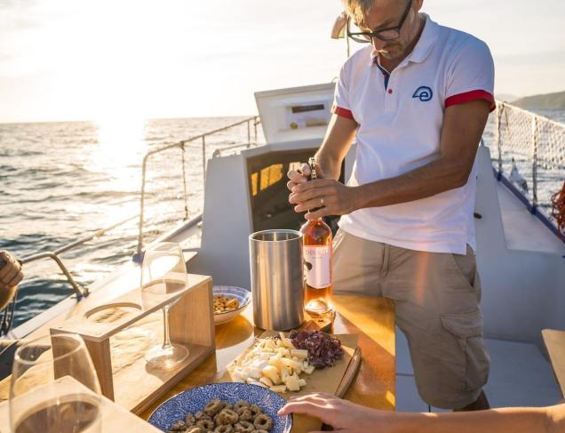 Degustazione di vino e prodotti tipici a bordo di una barca al tramonto sul mare.