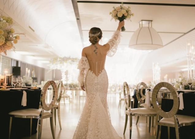 Sposa in abito da sirena in pizzo con bouquet di fiori, durante un elegante ricevimento nuziale.
