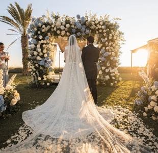 Matrimonio all’aperto al tramonto con sposi sotto un arco floreale bianco e azzurro.