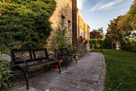 Giardino elegante e curato con panchine, vialetto in pietra e storica facciata in muratura, immerso nel verde.