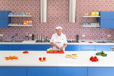 Cuoca prepara verdure fresche in una biberoneria professionale con arredi blu e pareti decorate.