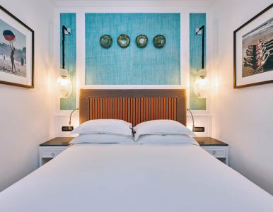 Camera da letto elegante con letto matrimoniale, testiera decorativa a righe arancioni e blu, parete turchese, applique luminose e dettagli di design raffinato.