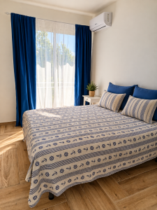 Camera da letto luminosa con letto matrimoniale, tende blu e bianche e biancheria in stile marinaro.