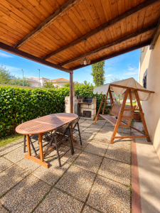 Ampio patio esterno arredato con tavolo e sedie in legno, dondolo coperto e barbecue in muratura.