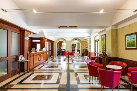 Elegante reception con arredi classici, pavimento in marmo e area lounge con poltrone rosse.