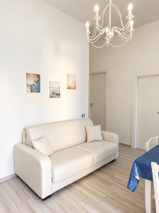 Soggiorno luminoso con divano bianco, elegante lampadario, tavolo da pranzo e arredi in tonalità neutre.
