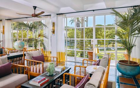 Veranda luminosa in stile tropicale con arredi in bambù, piante ornamentali e ampie vetrate sul giardino.