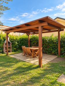 Giardino privato con pergolato in legno, tavolo e sedie da esterno, barbecue in muratura e siepe verde.