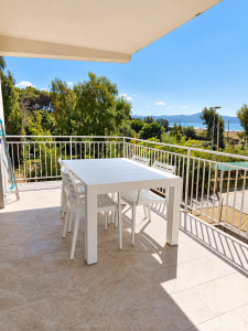 Terrazza panoramica vista mare con tavolo e sedie bianche, immersa nel verde.